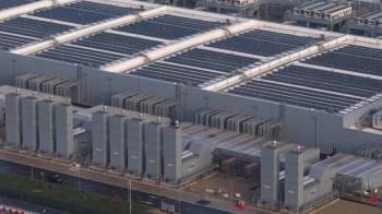 An industrial building of a data center featuring solar panels on the roof and large machinery units on the ground.