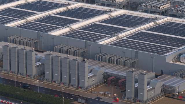 An industrial building of a data center featuring solar panels on the roof and large machinery units on the ground.