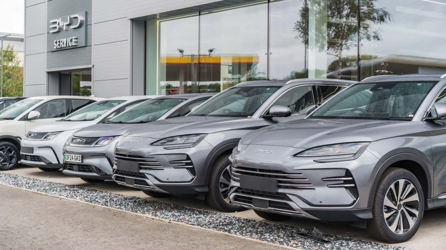 A row of various BYD vehicles parked outside a modern dealership, showcasing sleek designs and a contemporary building.