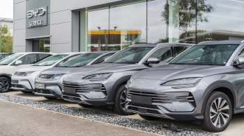A row of various BYD vehicles parked outside a modern dealership, showcasing sleek designs and a contemporary building.