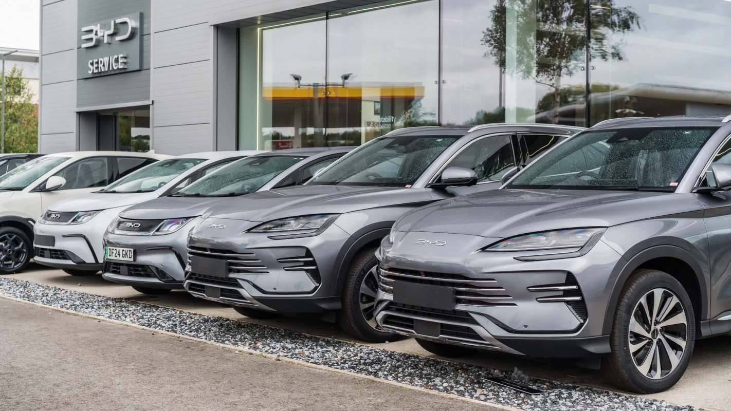 A row of silver and white BYD cars displayed in front of a service center.