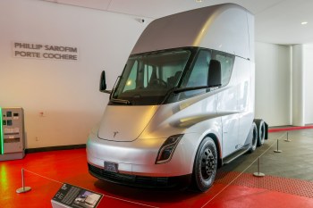 A Tesla semitruck on display in a modern exhibit space with a red floor.