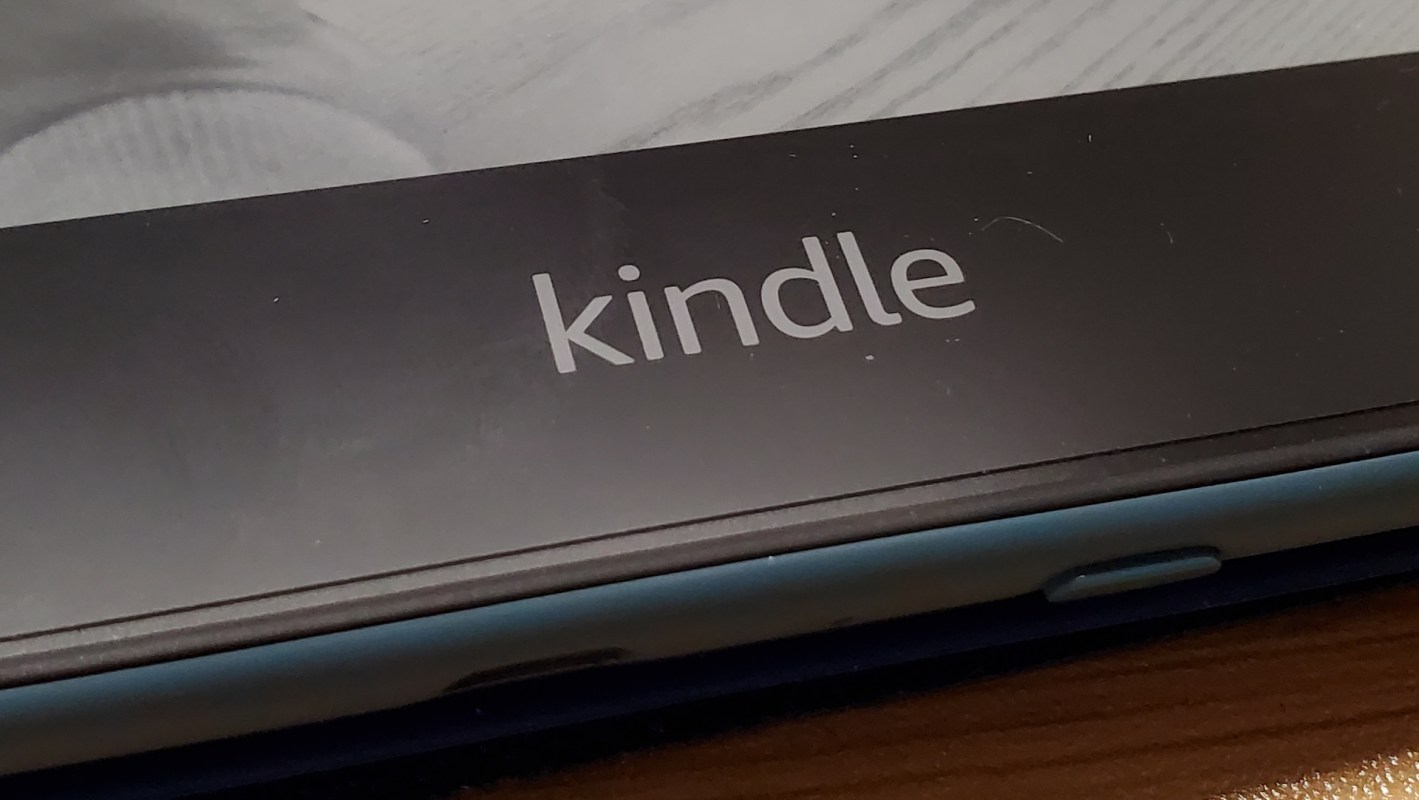 A close-up of a Kindle e-reader logo on a black background with a wooden surface underneath.