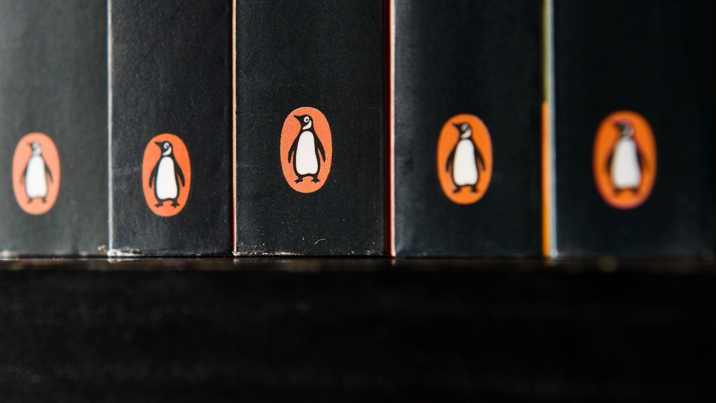 A row of book spines featuring the iconic Penguin Random House logo (black, white, and orange) against a dark background.