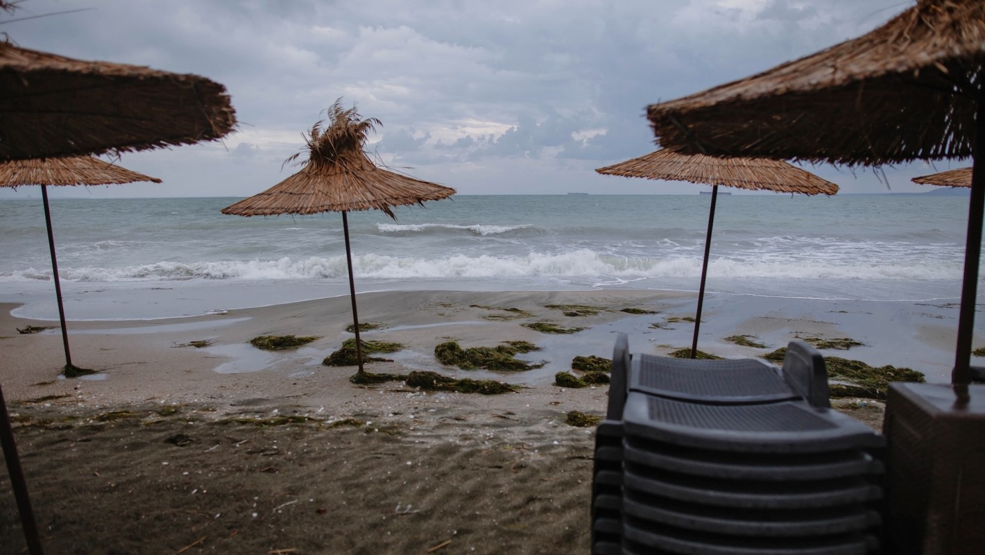 A beach scene featuring straw umbrellas, gentle waves, and seaweed on a cloudy day.