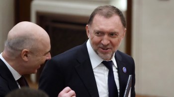 Russian businessman Oleg Deripaska share a light-hearted conversation with a man to his left.
