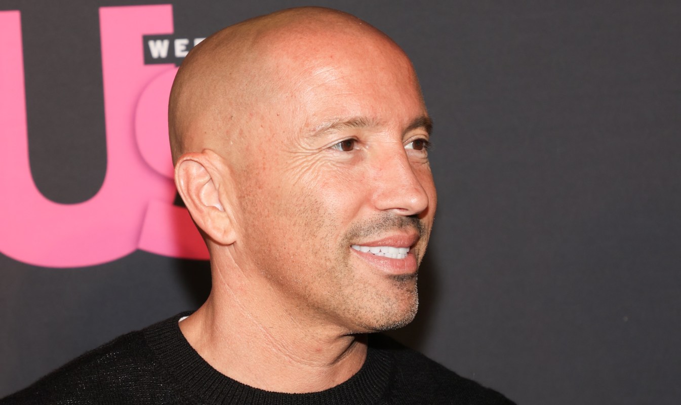 A close-up of Jason Oppenheim with a shaved head, smiling against a dark background with pink text.