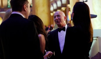 Jeff Bezos, at the right and in a tuxedo, talks with Elon Musk (left) during a formal event, surrounded by other guests.