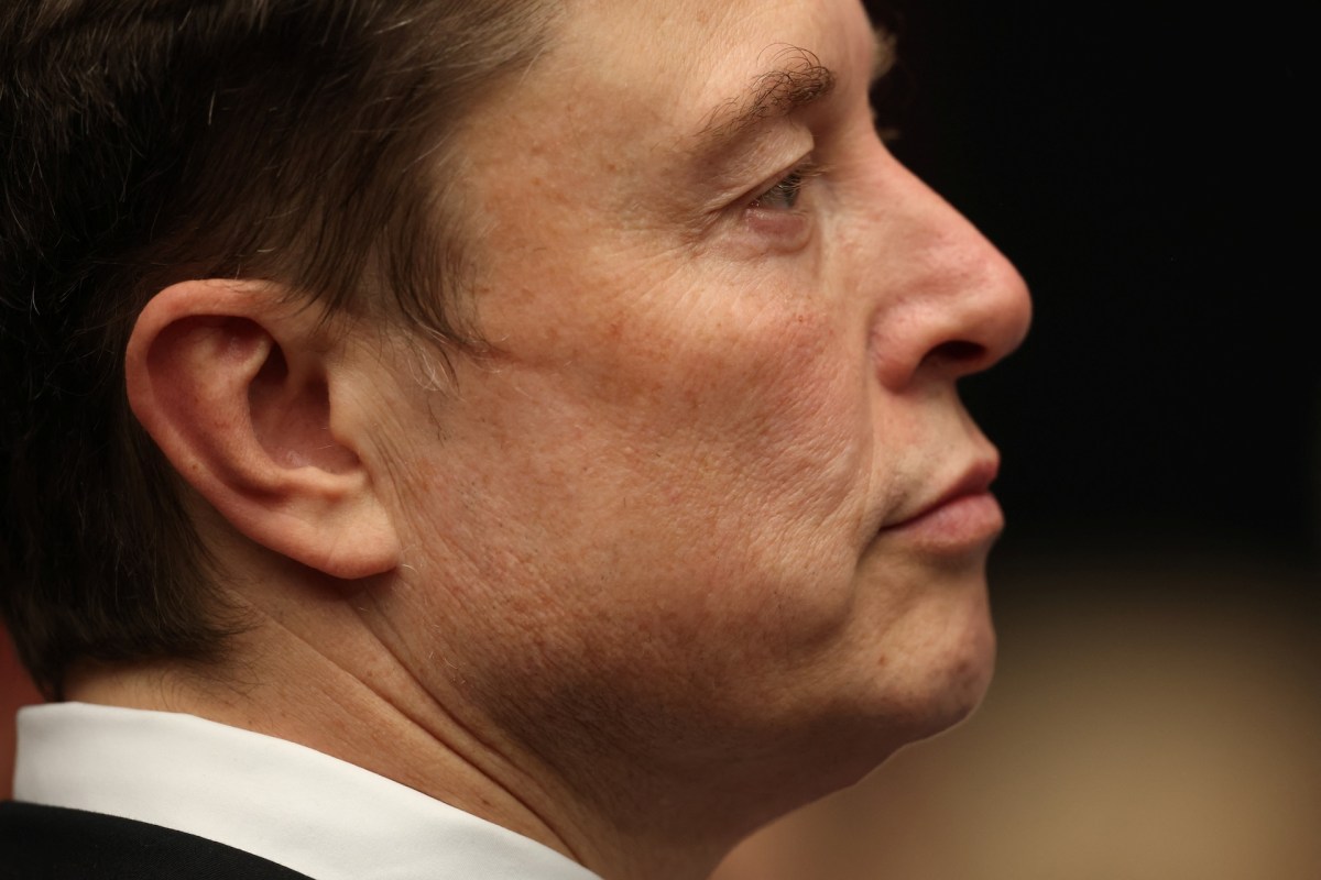 A close-up profile image of Elon Musk with short hair, wearing a black suit, looking contemplative.