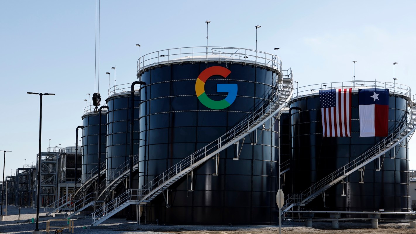 Three large black storage tanks as part of a data center with the Google logo and American and Texas flags displayed.
