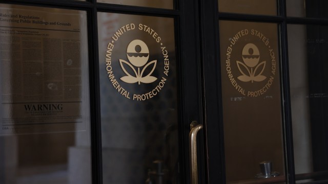 A close-up of the United States Environmental Protection Agency logo on glass doors with a warning sign visible.