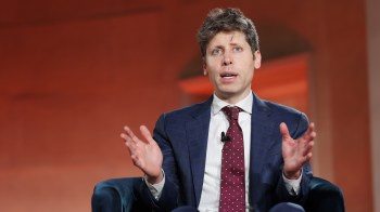 OpenAI CEO Sam Altman in a blue suit gestures while speaking during a discussion on a stage.