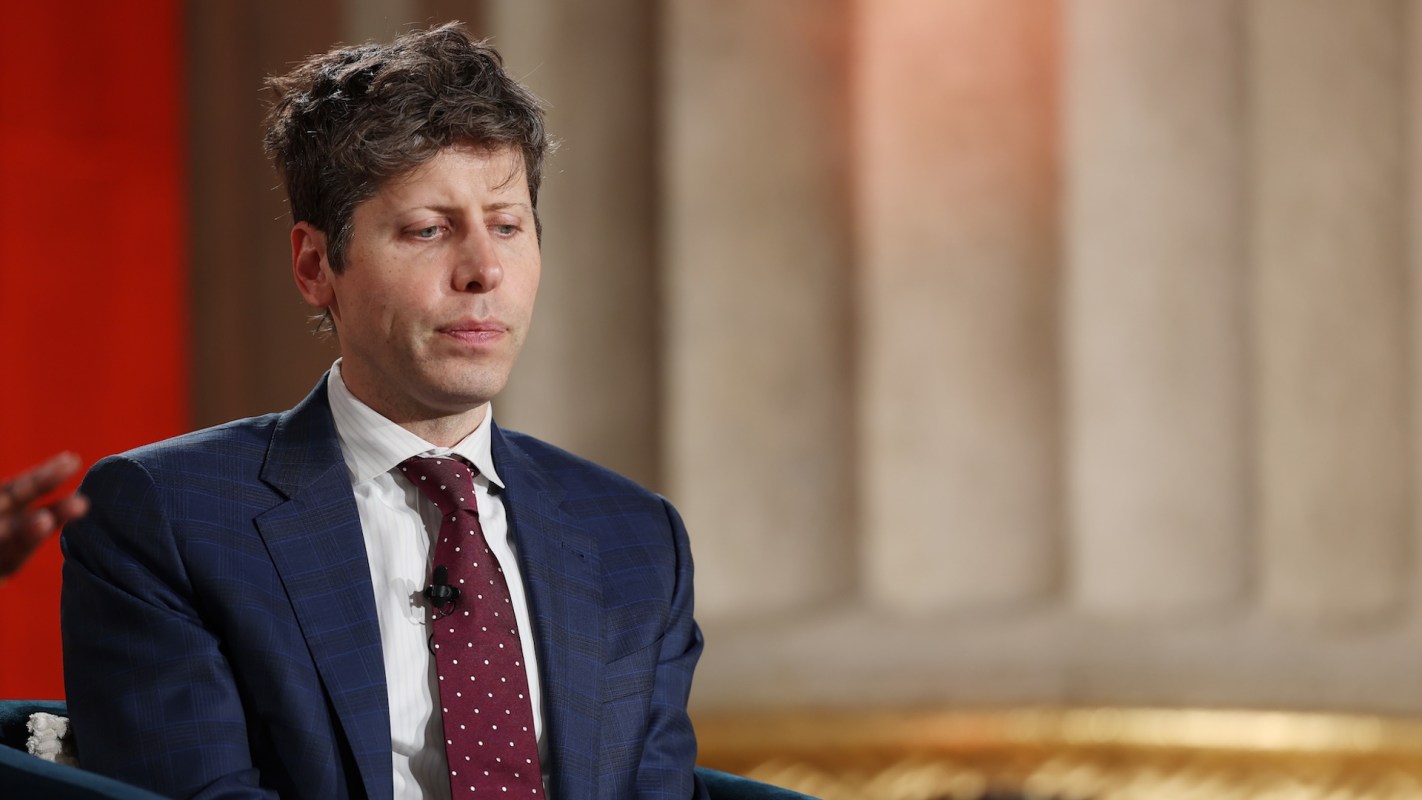 Sam Altman in a suit looks pensive while seated on stage during an event.