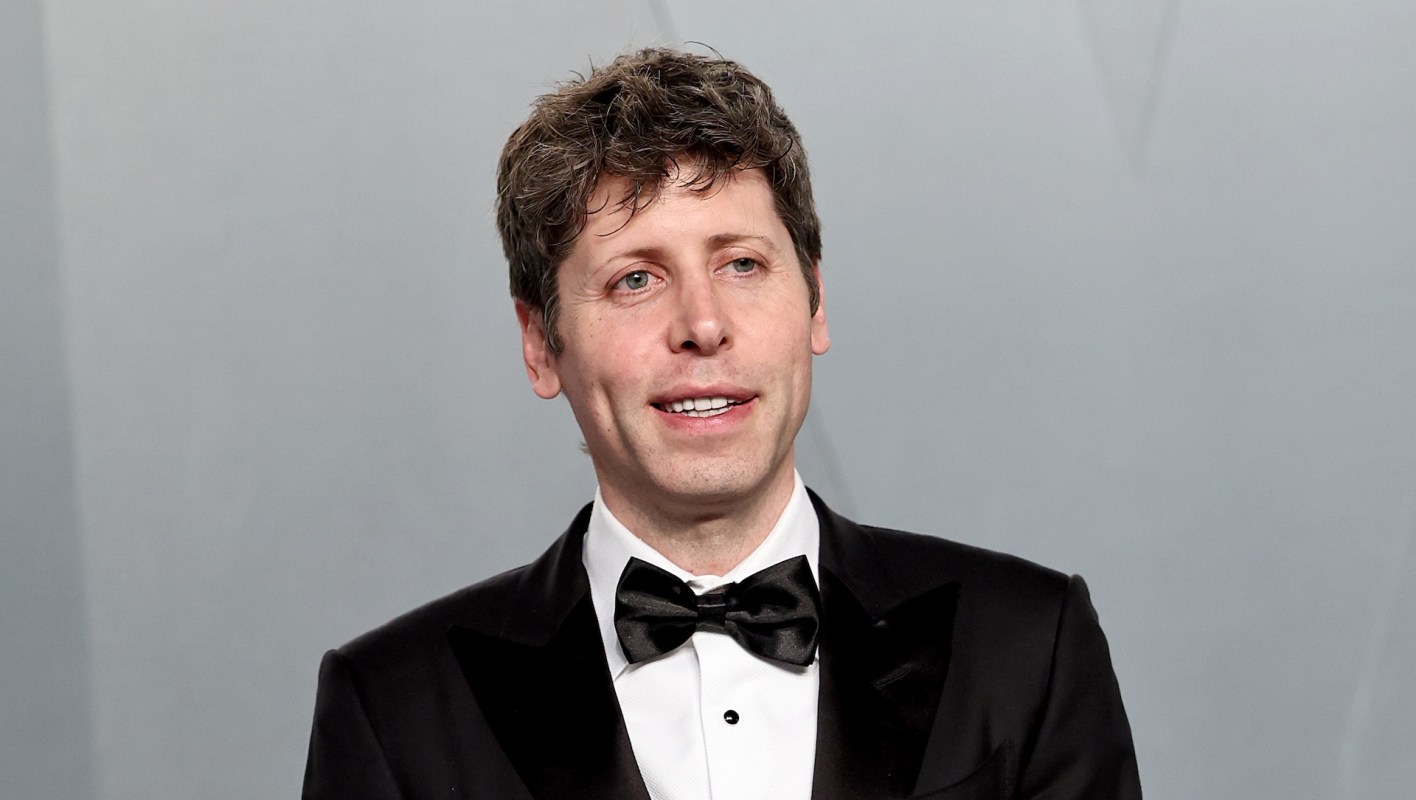 Sam Altman, in a tuxedo with a bow tie, smiles at the camera against a gray background.