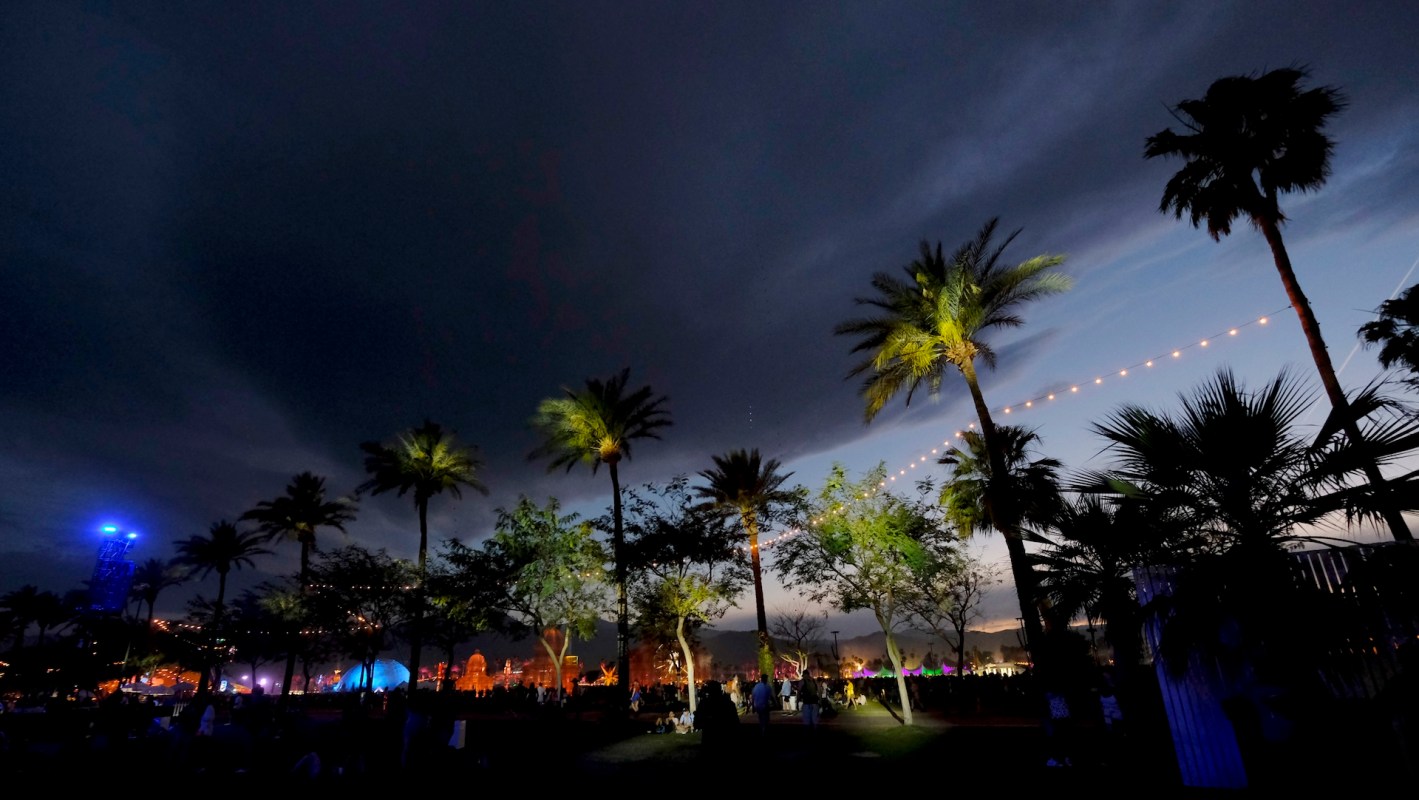 A vibrant outdoor event scene at dusk, with palm trees and colorful lights under a darkening sky.