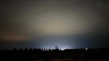 A dimly lit sky with subtle color gradients and distant lights peeking through silhouetted trees from a data center.