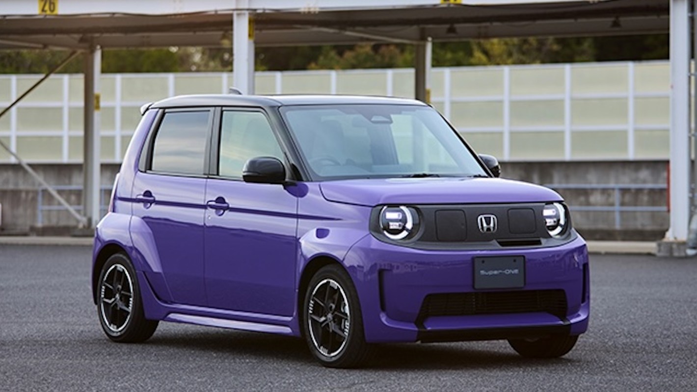 A compact purple Honda car parked in an empty lot with a modern backdrop and distinct headlights.