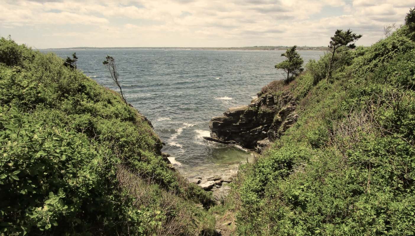 A serene coastal scene featuring green cliffs, rocky outcrops, and the ocean under a cloudy sky.