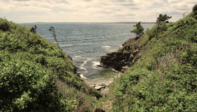 A serene coastal scene featuring green cliffs, rocky outcrops, and the ocean under a cloudy sky.