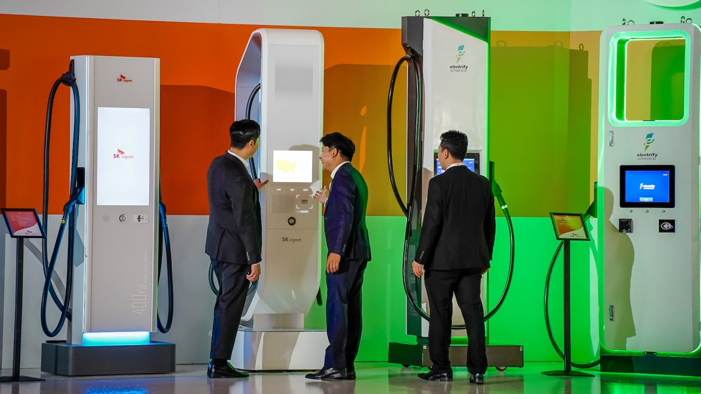 Three people in suits look at EV charging stations at a tech event.