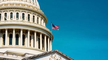 The U.S. Capitol dome topped with an American flag against a clear blue sky.