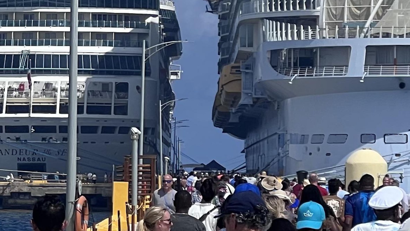 A crowded dock with large cruise ships on either side and people walking between them.
