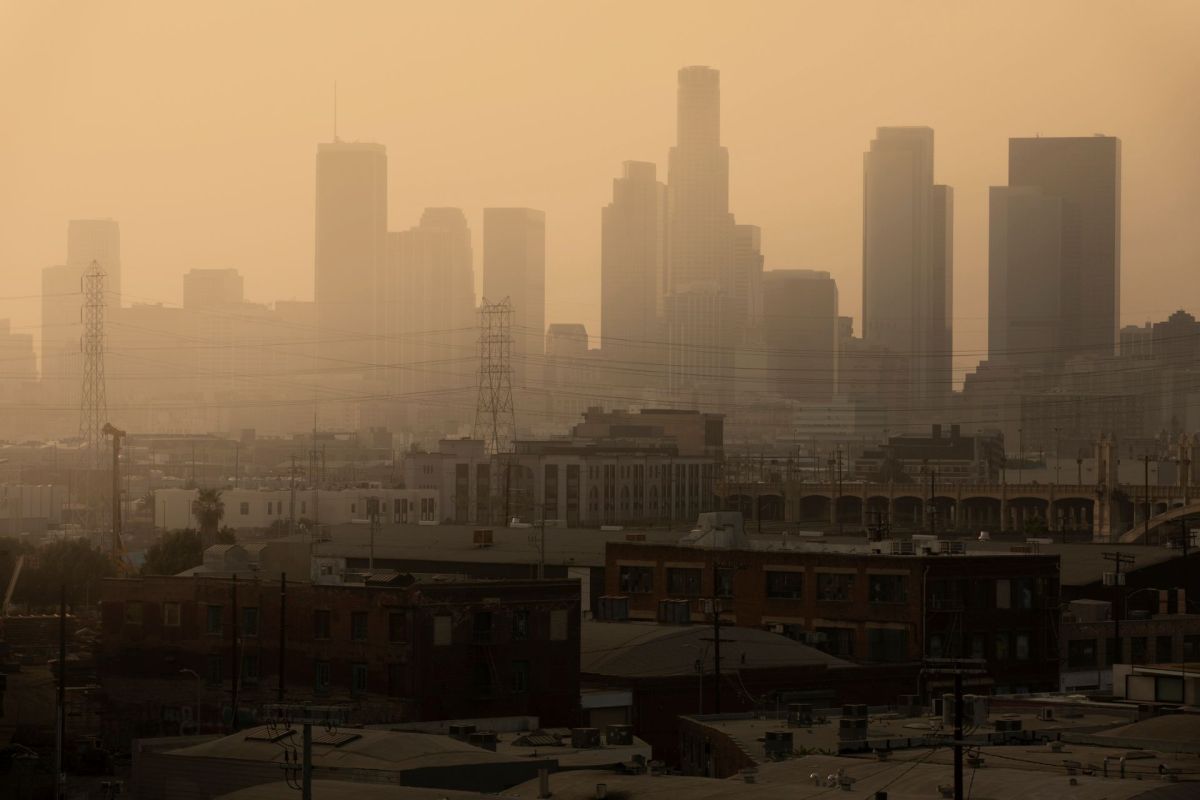 A hazy skyline of tall buildings in Los Angeles, with industrial structures in the foreground.