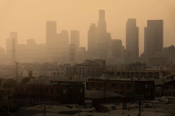 A hazy skyline of tall buildings in Los Angeles, with industrial structures in the foreground.