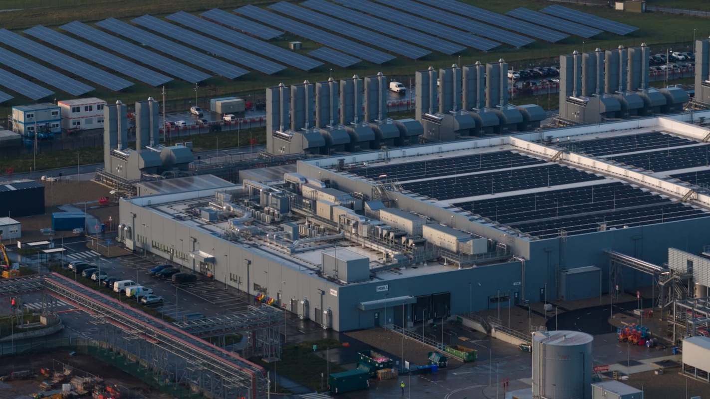 An aerial view of a data center with solar panels and large cooling towers.