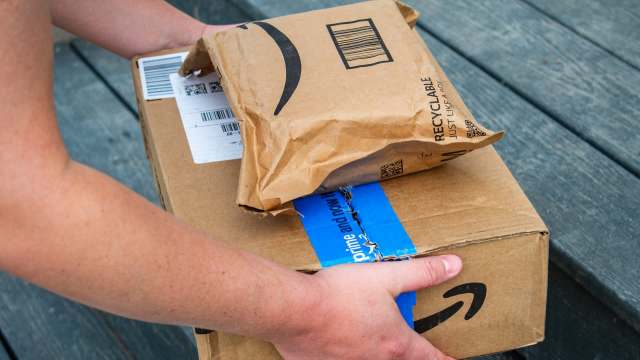 A person is holding two Amazon packages, one large and one small, on a wooden surface.