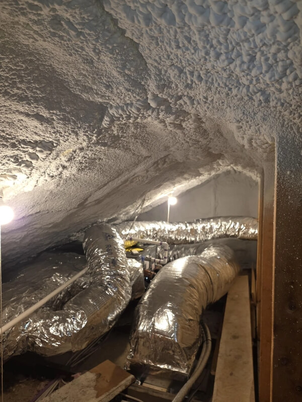 Shiny gray piping for a heat pump snakes through a tiny home's attic space. 