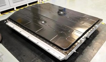 A large, flat sodium-ion battery pack with a metallic finish is situated on a workshop floor, surrounded by safety markings.