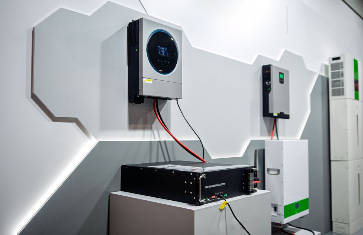 A modern battery storage system and cables with multiple inverters mounted on a gray wall.