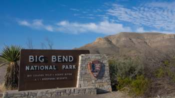 Sign for Big Bend National Park with rugged mountains and blue sky in the background.