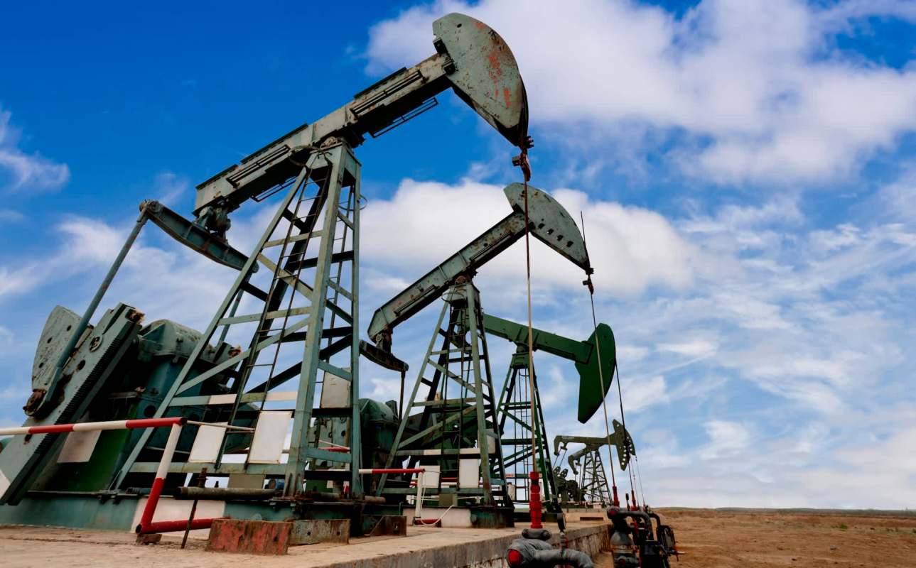 Oil pumps operate against a blue sky with scattered clouds in a rural landscape.