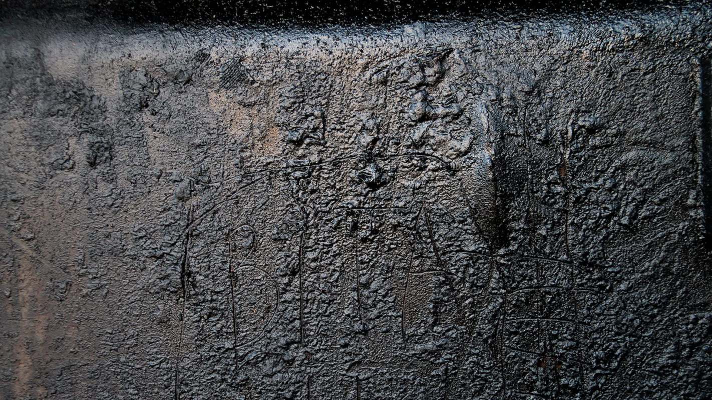 A textured black surface with a few faint scratches and markings.