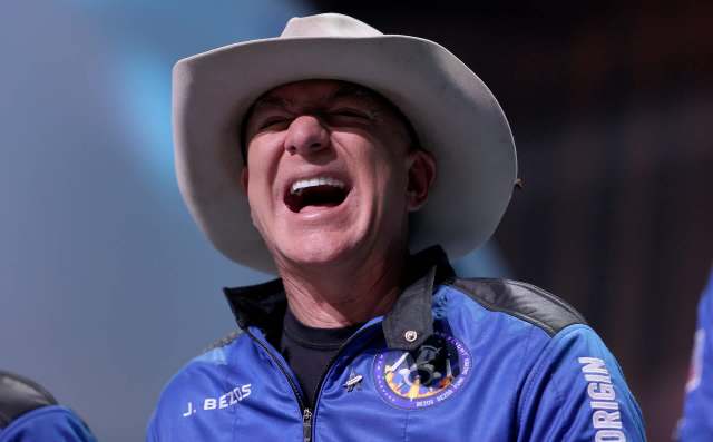 Jeff Bezos in a cowboy hat laughing while wearing a Blue Origin suit.