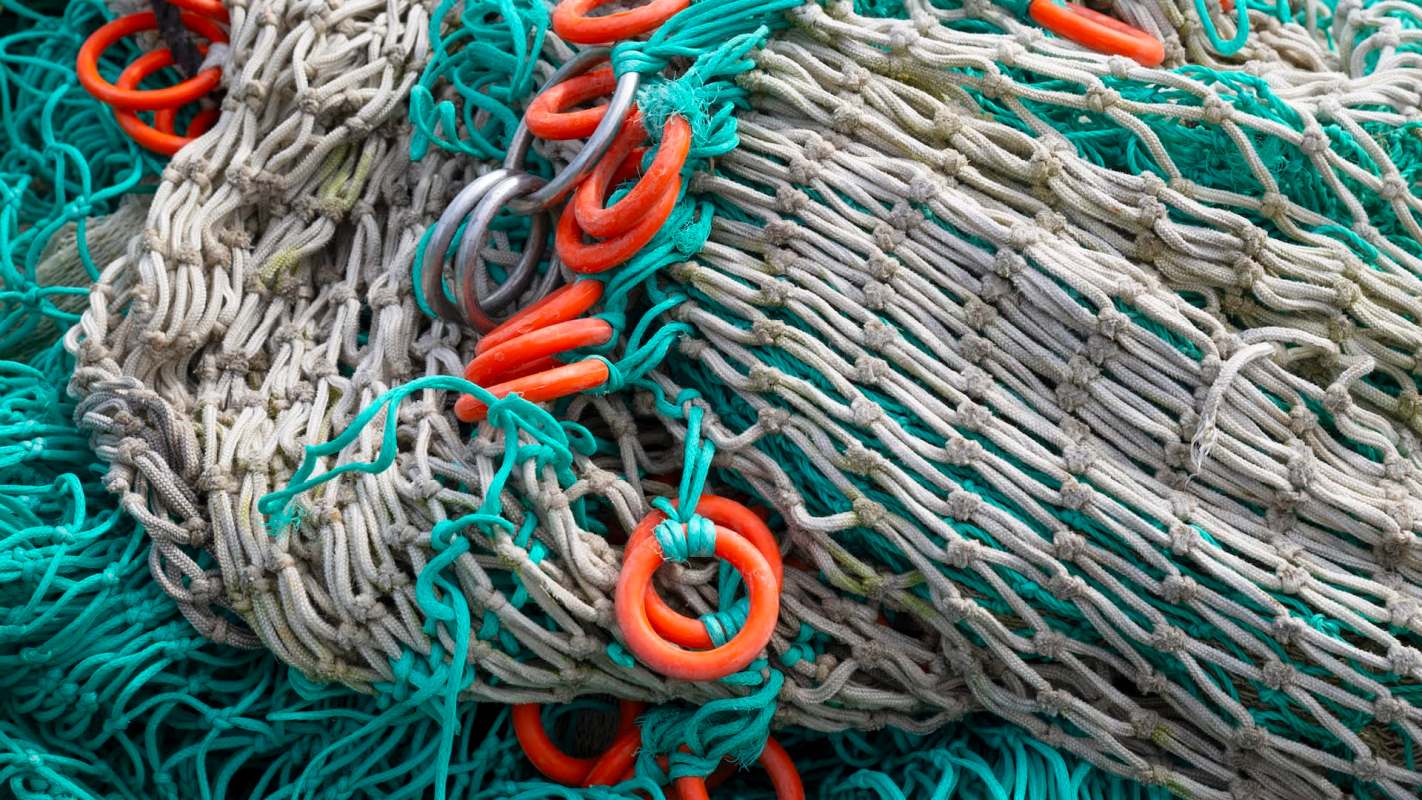 A close-up of fishing nets featuring intertwined fibers and bright orange rings among teal and beige threads.