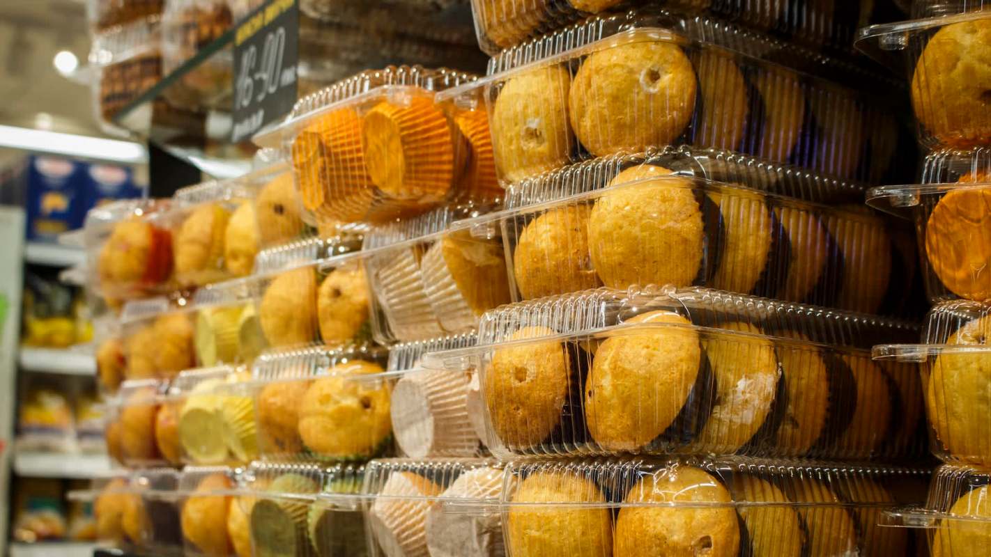 Stacks of transparent containers filled with various baked goods, including muffins and cupcakes, in a store display.
