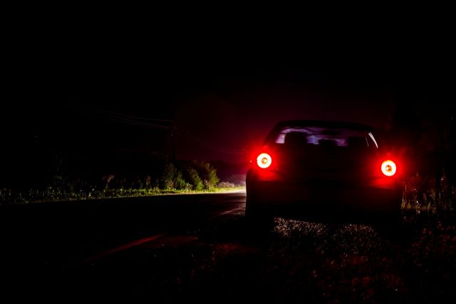 A car parked on a dimly lit roadside at night with red taillights.
