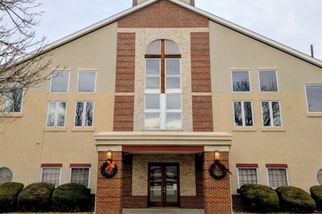 A modern church building featuring large windows and a prominent cross, decorated with wreaths.