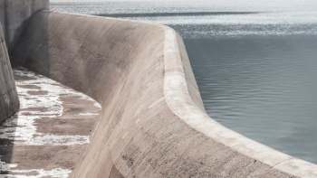 A curved concrete dam extends along a calm body of water, reflecting soft light.