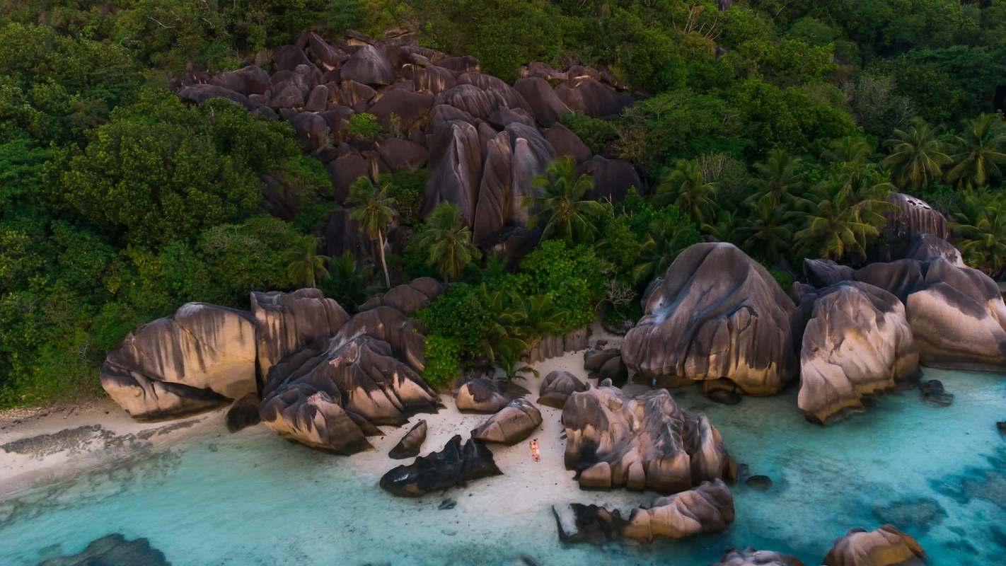 A beach with large rock formations, greenery, and blue waters.