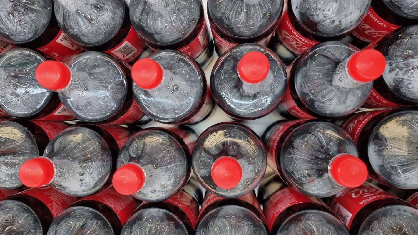 Aerial view of multiple Coke bottles with red caps arranged closely together.