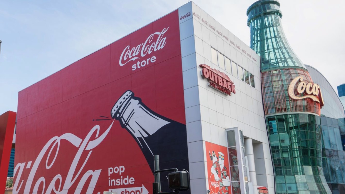 A Coca-Cola store featuring a large red exterior with a bottle graphic and an Outback Steakhouse sign nearby.