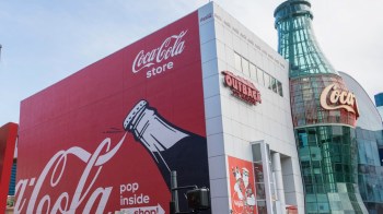 A Coca-Cola store featuring a large red exterior with a bottle graphic and an Outback Steakhouse sign nearby.