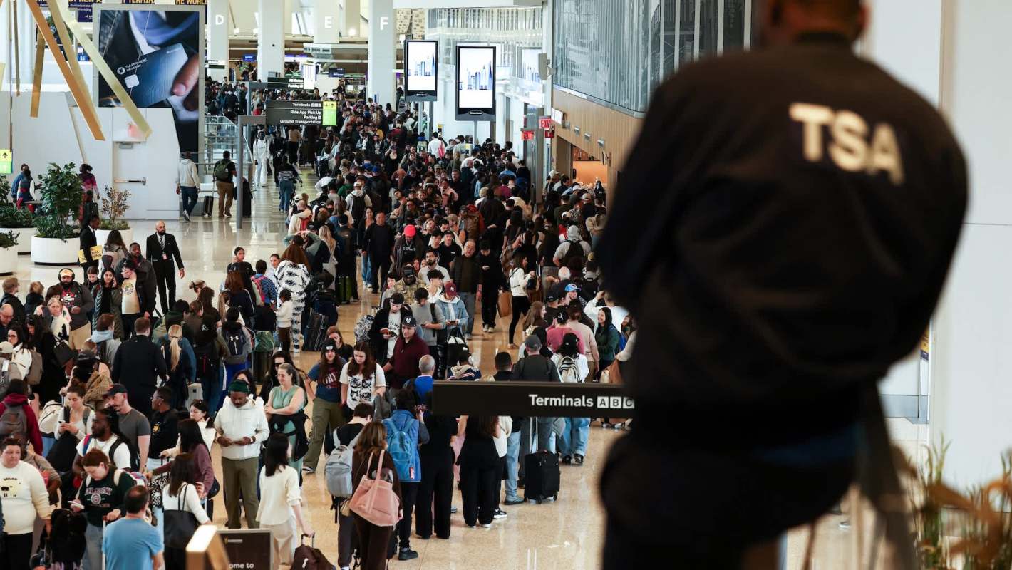 A crowded airport terminal with long lines of travelers and TSA personnel overseeing the security area.