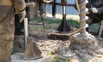 Workers using heavy machinery to drill into the ground at a construction site with dirt and tools visible.