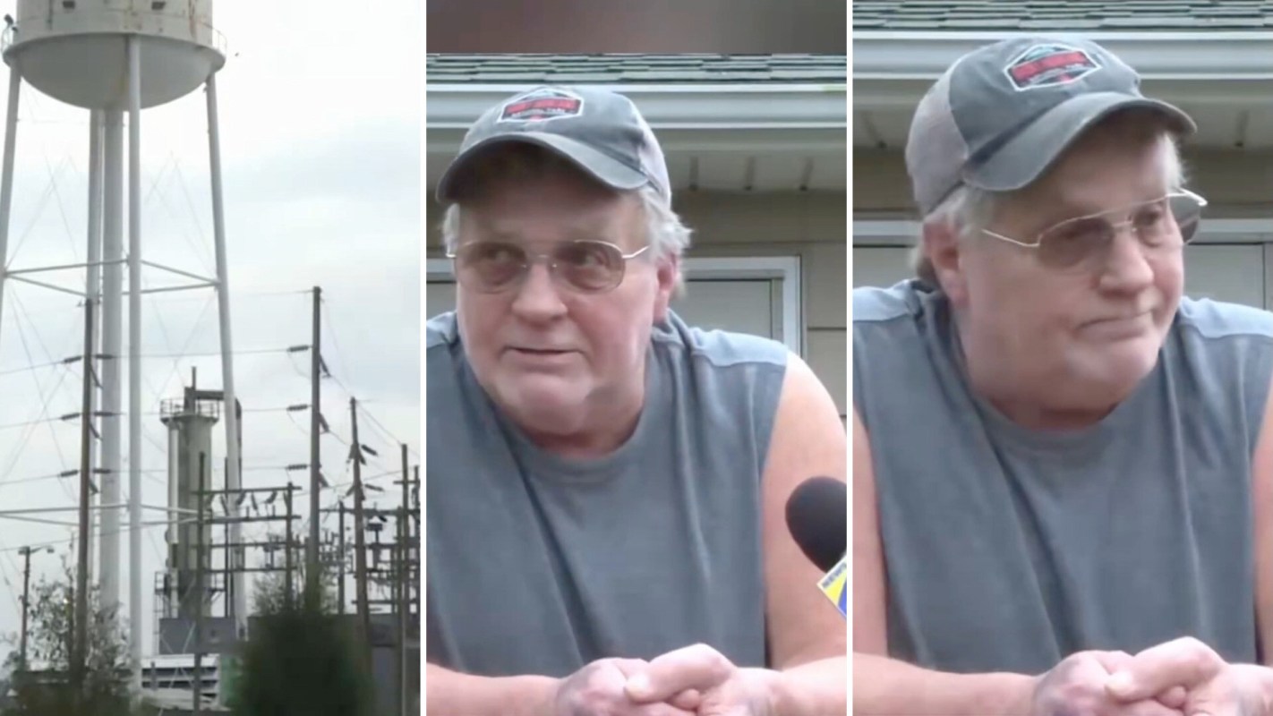 A man in a sleeveless shirt speaks in front of a water tower and power lines by a data center.