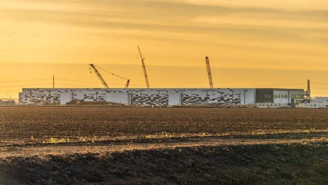 A large industrial building under construction with cranes against a golden sunset sky.
